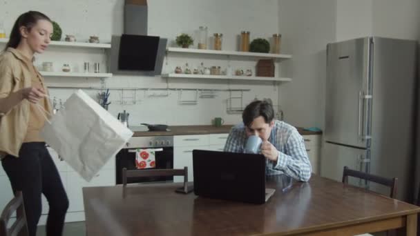 Жена ругает мужа, играющего на ноутбуке на кухне — стоковое видео
