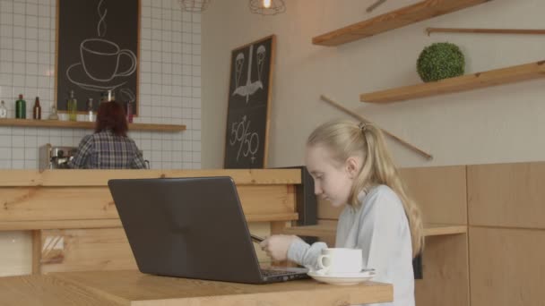 Malá holčička, která sedí u kavárny na stolku s notebookem — Stock video