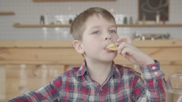 Маленький мальчик кладет картошку фри в рот в кафе — стоковое видео