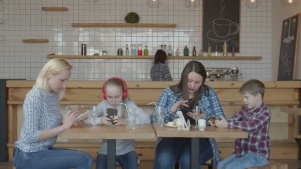 Femmes et enfants utilisant des téléphones se reposant à la table de café — Video