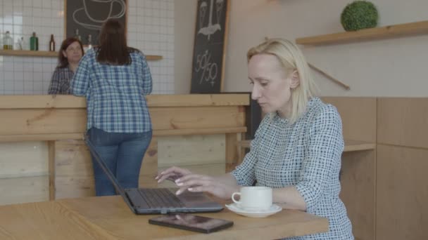 Серйозна жінка-блогер, що працює на ноутбуці в кафе — стокове відео