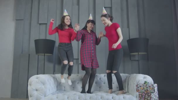 Mulheres alegres em chapéus de festa pulando no sofá — Vídeo de Stock