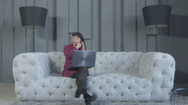 Занятая женщина работает на ноутбуке и телефоне дома — стоковое видео