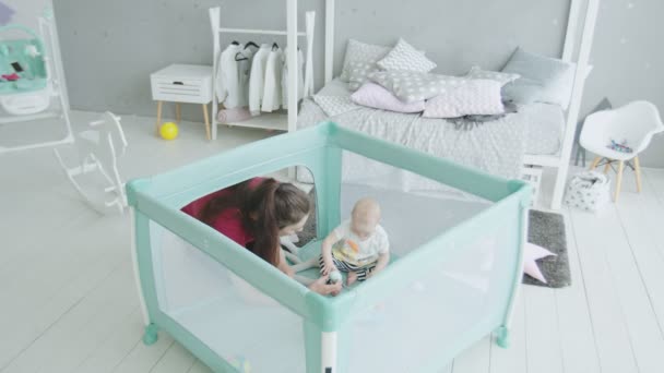 Liefdevolle moeder spelen met baby meisje in de kinderbox — Stockvideo