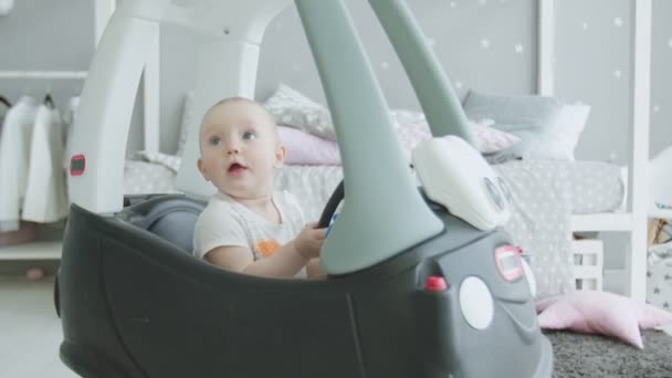 Alegre bebé mirando hacia arriba sentado en coche de juguete en casa — Vídeo de stock