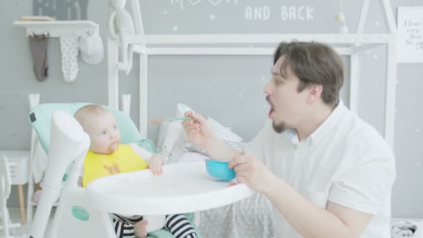 Father feeding baby sitting on high chair at home — Stock Video