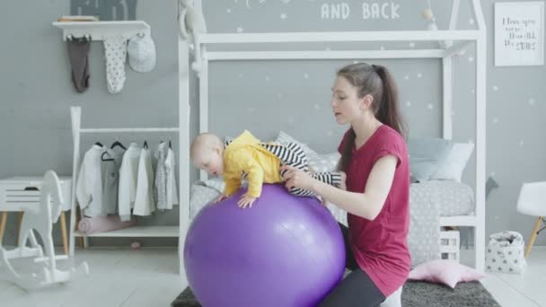 Jovem mãe balançando bebê menina no fitball em casa — Vídeo de Stock