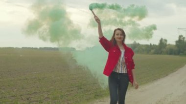 Kırsal yolda yürüyen kadın renkli dumanlar içinde kıvranıyor.