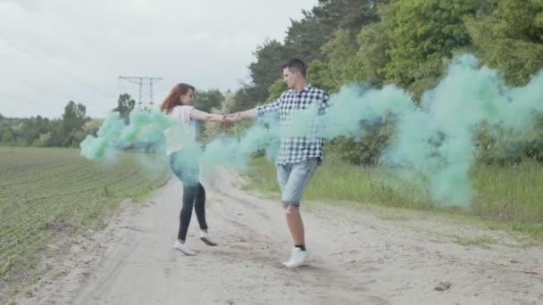 Pareja con humo de colores dando vueltas en la carretera polvorienta — Vídeos de Stock