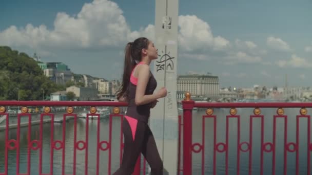 Chinese sporty female jogging along river bridge — Stock Video