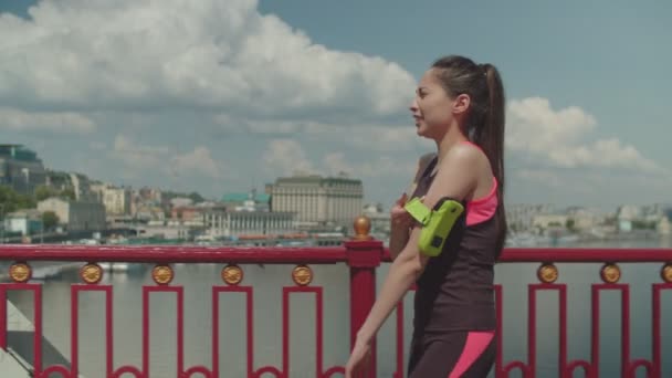 Mujer en forma tomando un descanso de entrenamiento caminando en el puente — Vídeo de stock