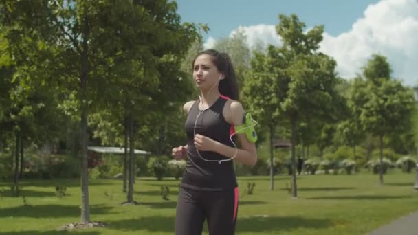 Fit mulher em fones de ouvido correndo na pista do parque — Vídeo de Stock