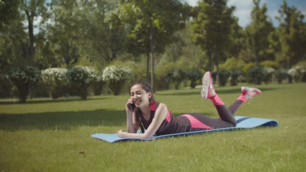 Fit vrouw praten op de telefoon liggend op mat buitenshuis — Stockvideo