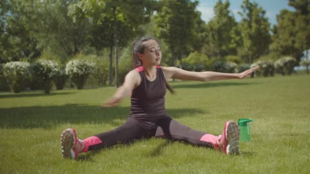 Asiática mujer entrenamiento músculos sentado en parque césped — Vídeo de stock