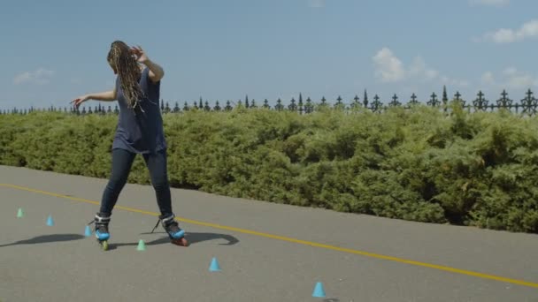 Женщина катается на роликах назад через конусы на открытом воздухе — стоковое видео