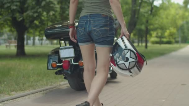 Женщина идет к мотоциклу со шлемом в руке — стоковое видео