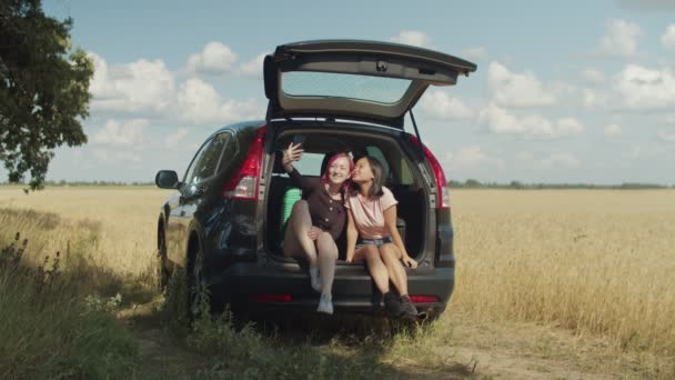 Joyful female friends taking selfie in car trunk — Stock Video