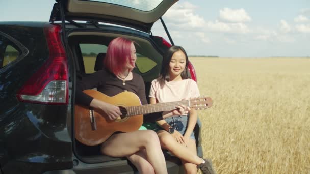Hipster women playing guitar sitting in car trunk — Stock Video