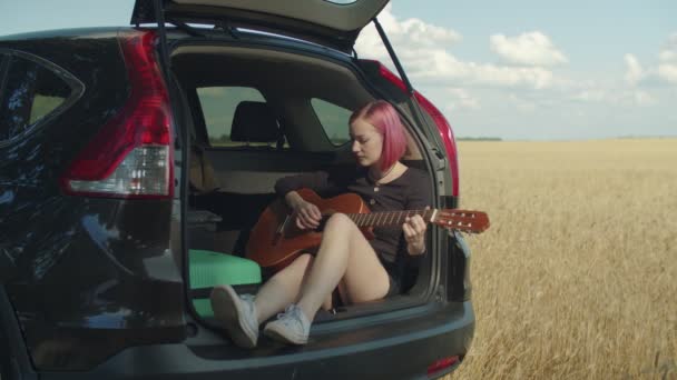Dreamy hipster woman playing guitar in car trunk — Stock Video