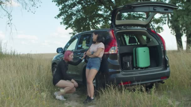 Viajeros femeninos revisando neumáticos pinchados en coche — Vídeos de Stock