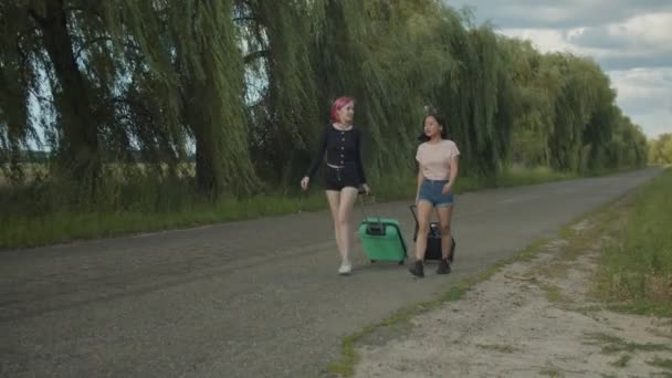 Mulheres turistas com sacos de viagem caminham na estrada rural — Vídeo de Stock