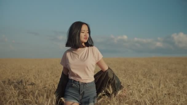 Vrolijke Aziatische vrouw wandelen in tarwe veld bij zonsondergang — Stockvideo