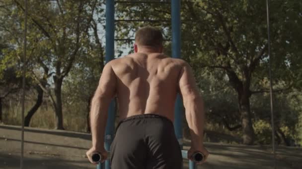 Fit hombre haciendo salpicaduras de tríceps en barras paralelas al aire libre — Vídeo de stock