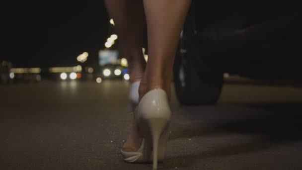 Женщина в туфлях на высоком каблуке садится ночью в машину — стоковое видео