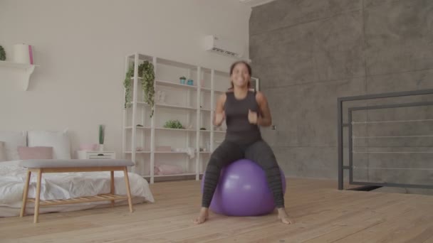 Glückliche Afrikanerin trainiert auf Fitball drinnen — Stockvideo