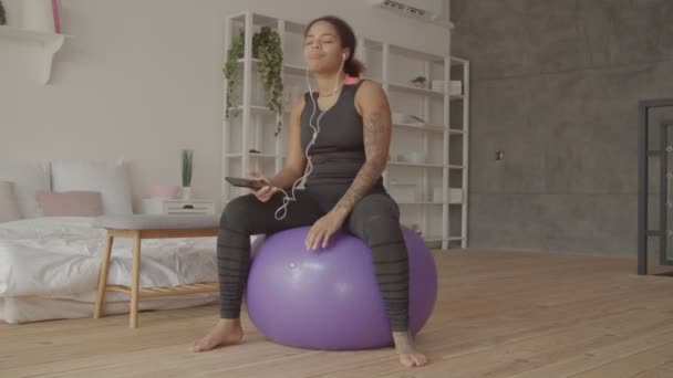 Mujer positiva en fitball escuchando música en el teléfono — Vídeos de Stock