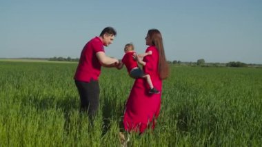 Aile tarlada yürüyor, küçük kızı kaldırıyor.