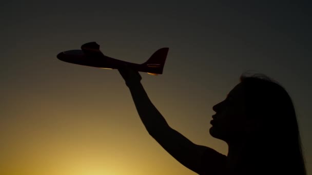 Sylwetka kobiecej dłoni z zabawkowym samolotem o zachodzie słońca — Wideo stockowe