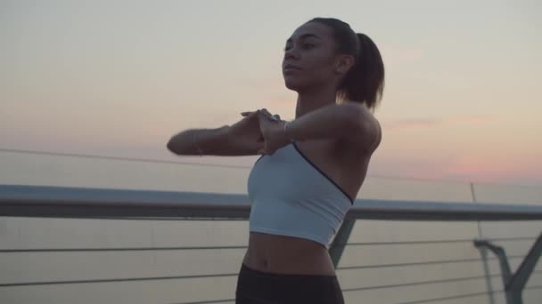 Black fit female runner stretching arms at sunrise — Stock Video