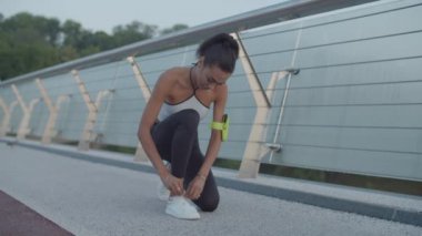 Şafak vakti koşu yaparken ayakkabı bağlayan atlet kadın.