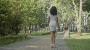 Yüksek topuklu ayakkabılı bir kadının parkta yürümesi.