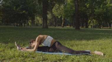 Esnek bir kadın yoga minderini açık havada ikiye ayırıyor.