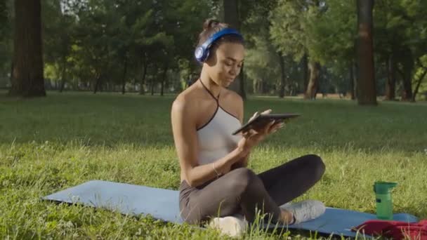 Vrouw in hoofdtelefoon met tablet pc ontspannen buiten — Stockvideo