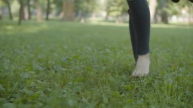 Çıplak ayaklı kadın bacakları parkta yeşil çimlerde yürüyor.