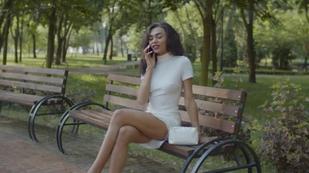 Ganska svart kvinna pratar på mobiltelefon på bänken — Stockvideo