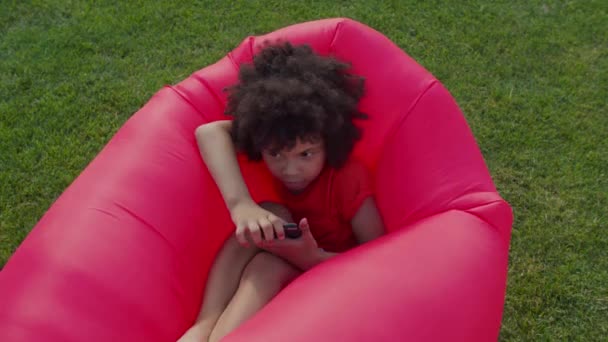 Söt liten pojke med telefon vilar på luft solstol — Stockvideo