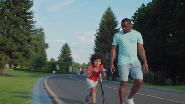 Joyful pequeno filho montando empurrar scooter no parque — Vídeo de Stock