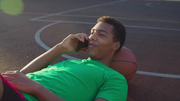 Спортсмен спілкується по телефону на баскетбольному майданчику — стокове відео