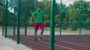 Ciddi bir sokak basketbolcusu sahada top sürüyor.