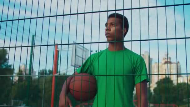 Jogador de basquete pensivo segurando bola na quadra urbana — Vídeo de Stock