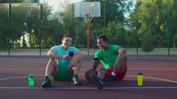 Atletas com telefones descansando na quadra de basquete — Vídeo de Stock