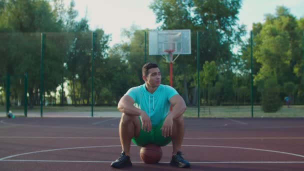 Jogador de streetball relaxado sentado no basquete — Vídeo de Stock