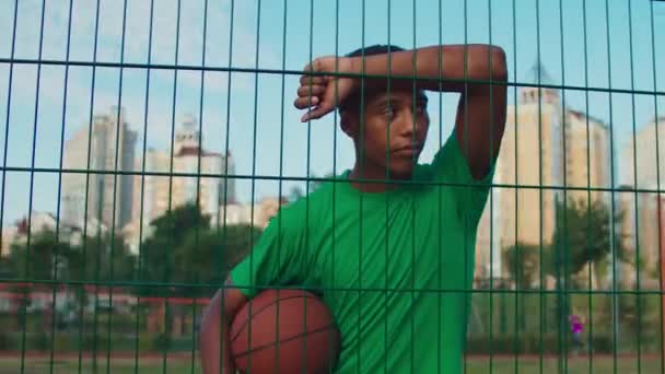 Atleta com basquete apoiado em cerca esportiva — Vídeo de Stock