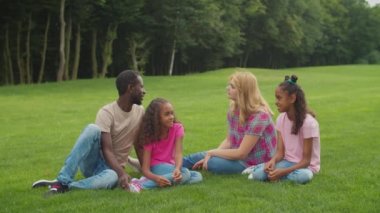 Kızları yeşil çimlerde dinlenen çeşitli aileler.