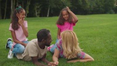 Farklı aileler çimenlerde yatar, kızlar da sırtında.