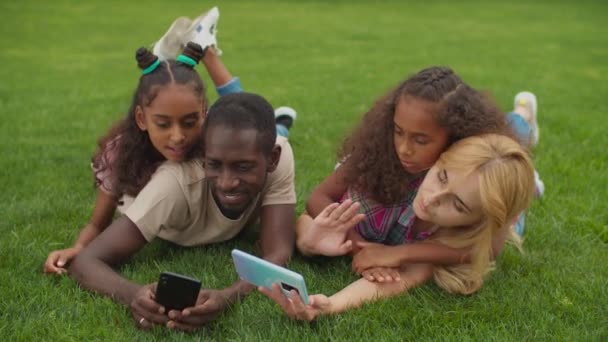 Keluarga multirasial mengambil selfie berbaring di rumput — Stok Video
